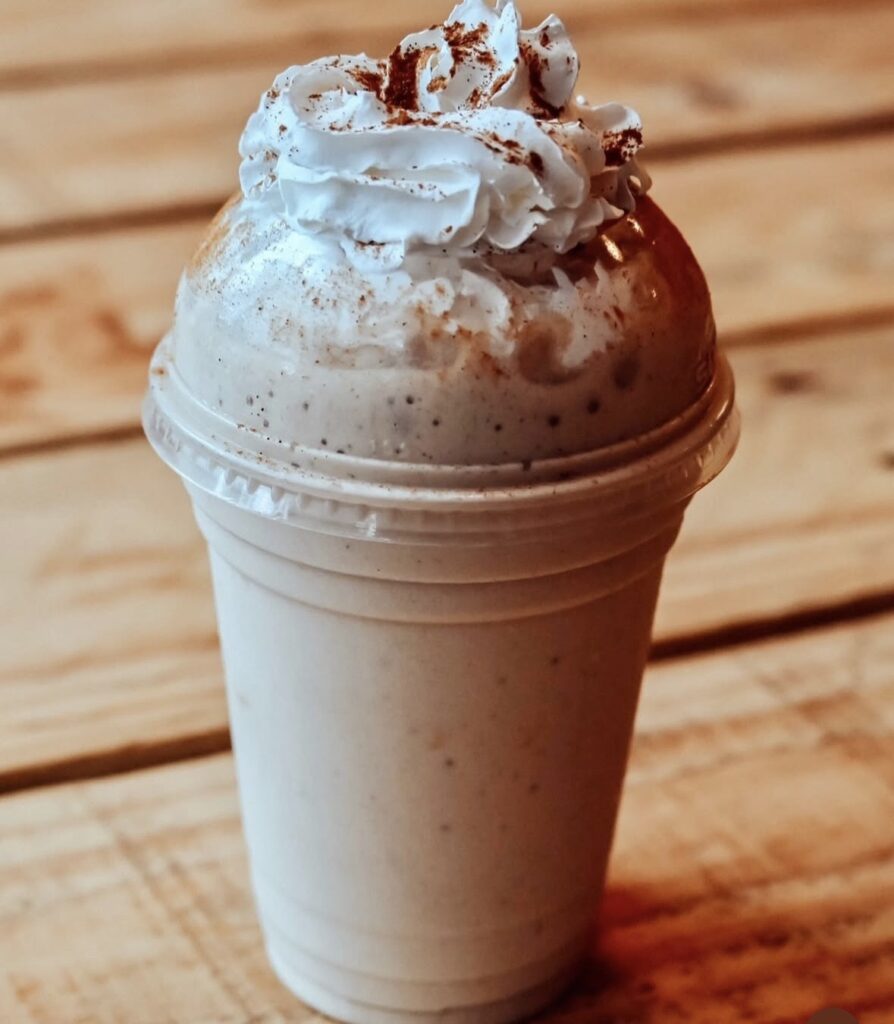 Delicious beige caramel protein shake topped with whipped cream and a light caramel drizzle, served in a medium cup.